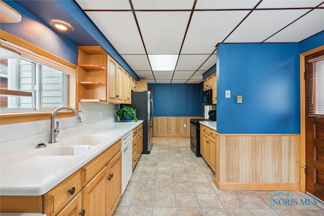 kitchen featuring a drop ceiling, sink, black appliances, light tile patterned floors, and wood walls