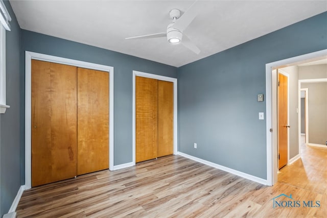 unfurnished bedroom with ceiling fan, light hardwood / wood-style floors, and two closets