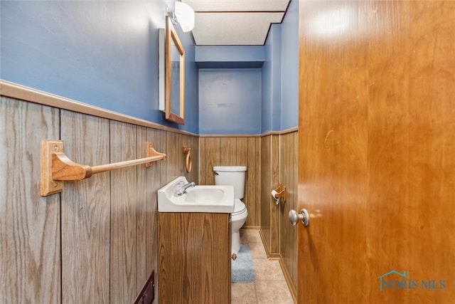 bathroom featuring tile patterned floors, vanity, toilet, and wooden walls