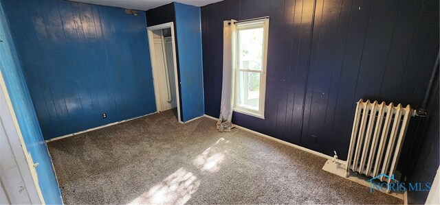 spare room with radiator, wood walls, and carpet floors