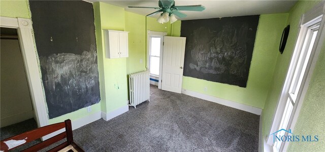 unfurnished bedroom with dark colored carpet, radiator, and ceiling fan