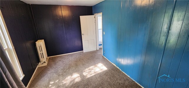 carpeted spare room with wood walls and radiator heating unit