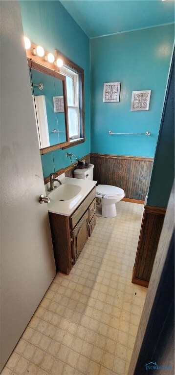 bathroom featuring vanity, toilet, and wooden walls