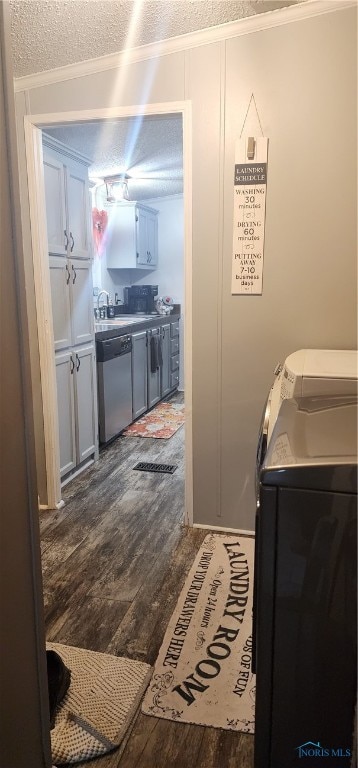 laundry room featuring cabinets, dark hardwood / wood-style floors, ornamental molding, a textured ceiling, and washing machine and clothes dryer