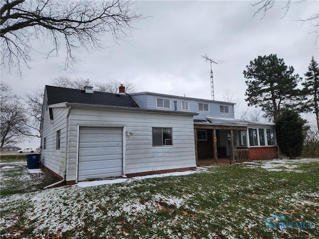 snow covered rear of property with a lawn, a sunroom, and a garage