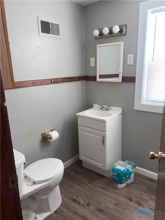 bathroom with a wealth of natural light, wood-type flooring, and tile walls