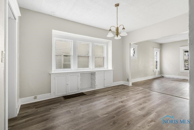 unfurnished dining area featuring dark hardwood / wood-style flooring, a textured ceiling, and an inviting chandelier