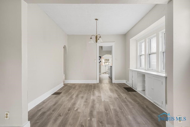 unfurnished dining area with a chandelier, a textured ceiling, and light hardwood / wood-style floors