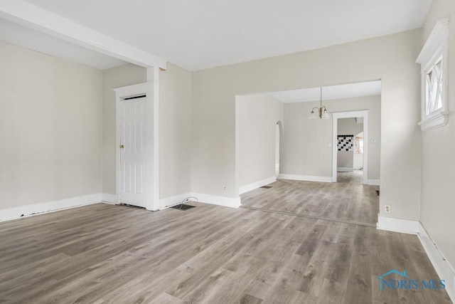 empty room featuring wood-type flooring and a chandelier