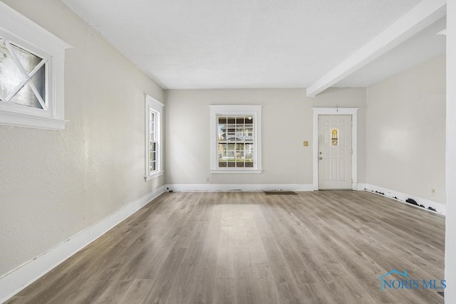 unfurnished living room featuring hardwood / wood-style floors and beamed ceiling