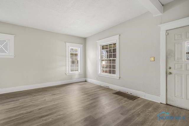 empty room featuring hardwood / wood-style floors, beam ceiling, and a textured ceiling