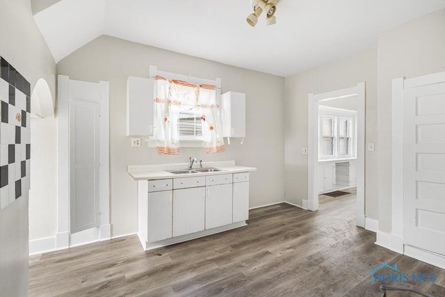 kitchen featuring sink, white cabinets, hardwood / wood-style floors, and vaulted ceiling