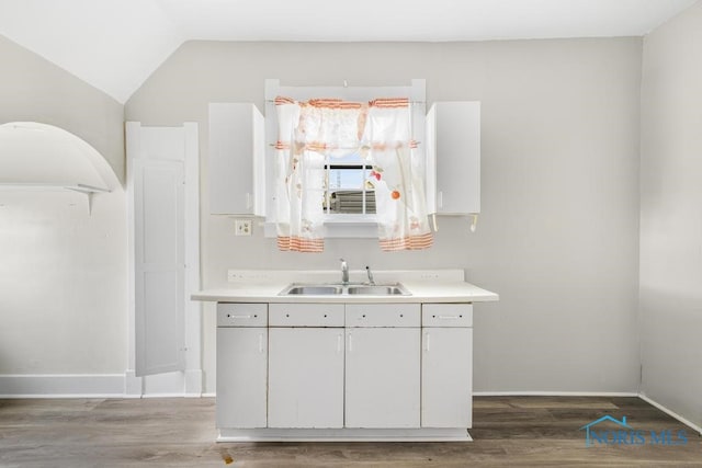 interior space with dark hardwood / wood-style floors, vaulted ceiling, white cabinetry, and sink