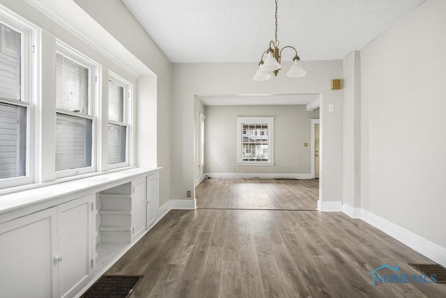 unfurnished dining area with hardwood / wood-style floors, a textured ceiling, and a chandelier