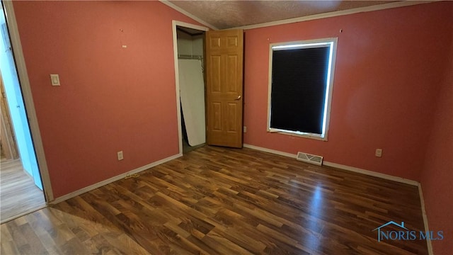 unfurnished bedroom featuring dark hardwood / wood-style floors, crown molding, a textured ceiling, and vaulted ceiling