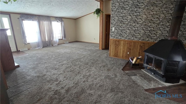 carpeted living room featuring wood walls, crown molding, a wood stove, and a textured ceiling