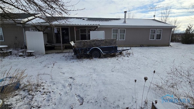 snow covered rear of property featuring a sunroom