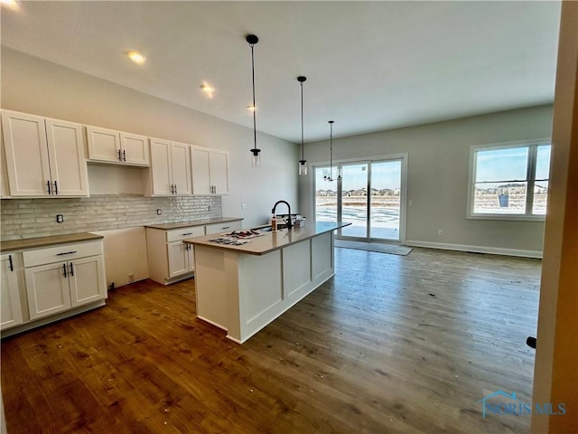 kitchen featuring decorative light fixtures, dark wood-type flooring, an island with sink, and white cabinets