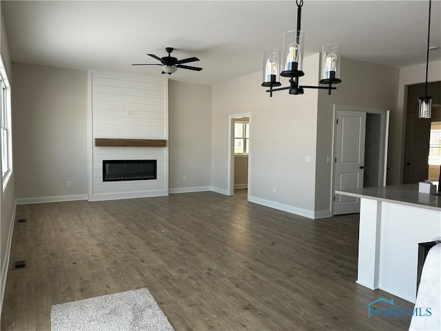 unfurnished living room featuring dark wood-type flooring, a fireplace, and ceiling fan with notable chandelier