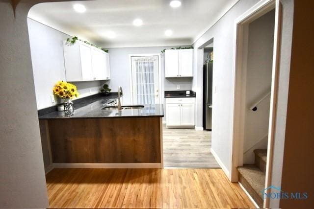 kitchen featuring white cabinets, stainless steel fridge, light wood-type flooring, and sink