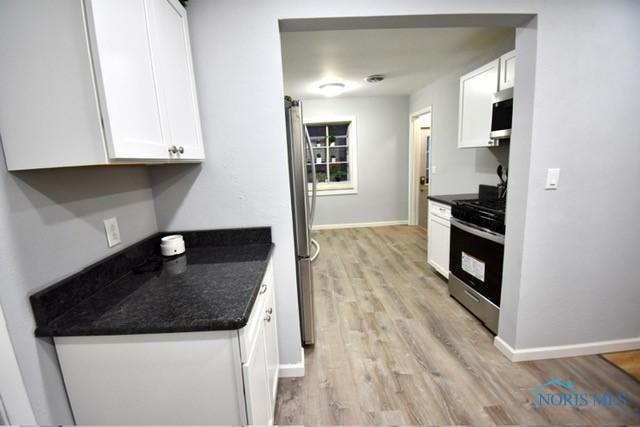 kitchen with white cabinets, light wood-type flooring, stainless steel appliances, and dark stone countertops