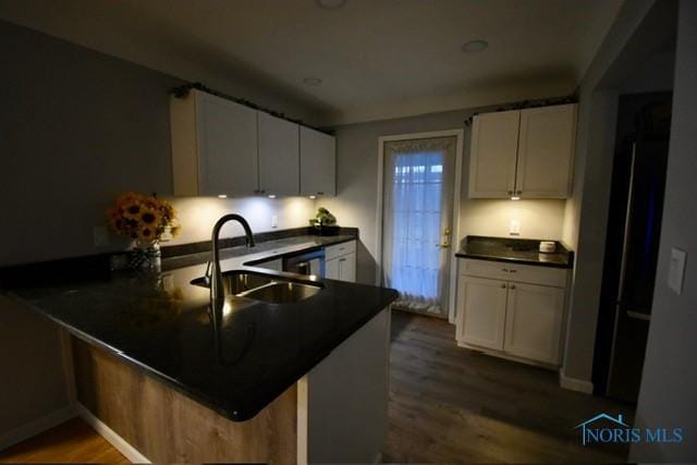 kitchen with kitchen peninsula, dishwashing machine, dark wood-type flooring, sink, and white cabinets