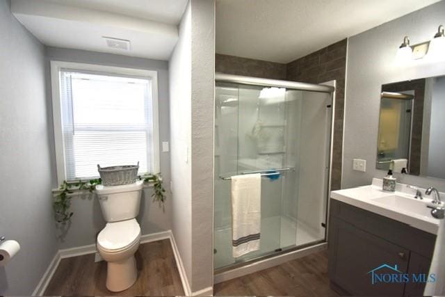 bathroom featuring hardwood / wood-style floors, vanity, a shower with shower door, and toilet