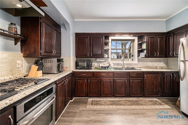 kitchen with sink, wall chimney exhaust hood, stainless steel appliances, tasteful backsplash, and light wood-type flooring