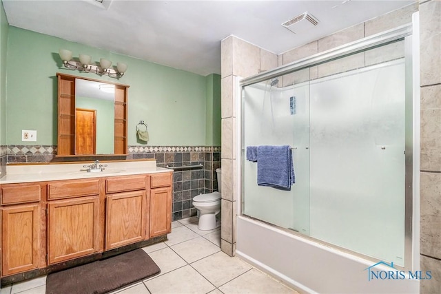 full bathroom with vanity, shower / bath combination with glass door, tile patterned floors, toilet, and tile walls