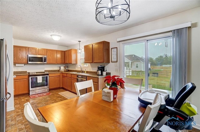 kitchen with a textured ceiling, stainless steel appliances, sink, pendant lighting, and an inviting chandelier