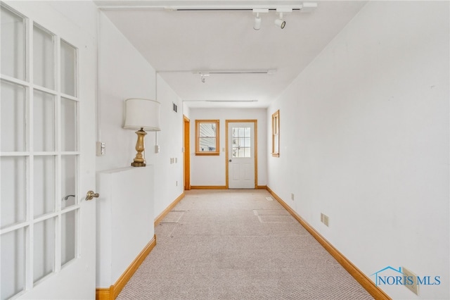 doorway to outside featuring light carpet and rail lighting