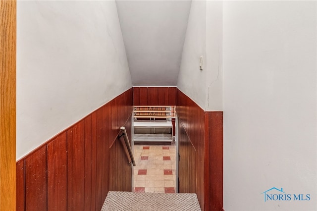 stairs featuring vaulted ceiling and wood walls