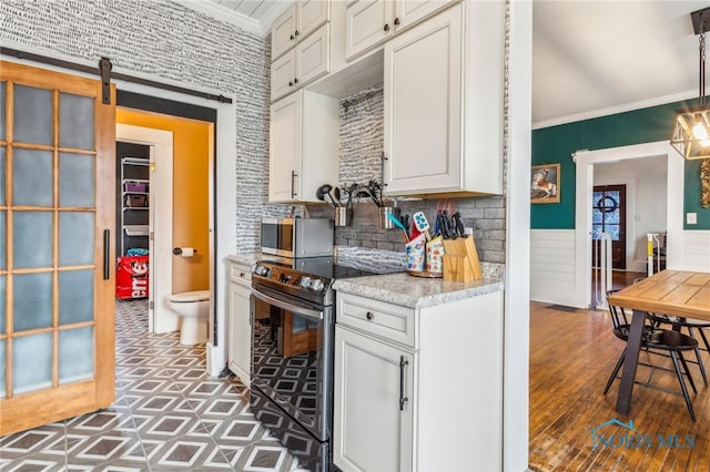 kitchen featuring white cabinets, electric range oven, a barn door, and crown molding