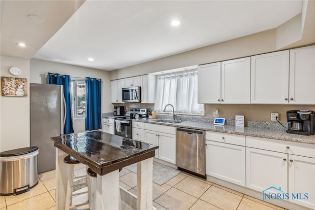 kitchen featuring light stone countertops, white cabinetry, sink, stainless steel appliances, and light tile patterned floors