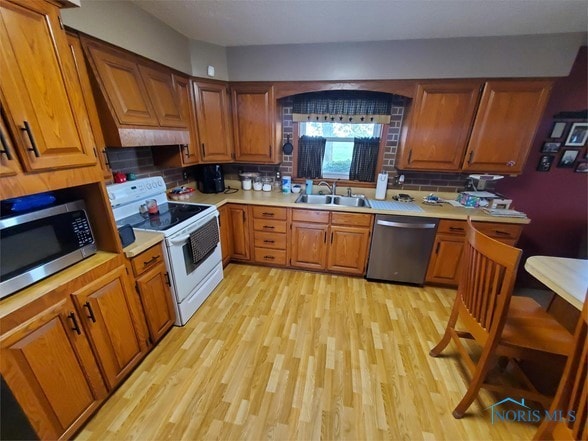 kitchen featuring backsplash, sink, stainless steel appliances, and light wood-type flooring