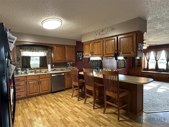 kitchen featuring a kitchen bar, stainless steel dishwasher, a textured ceiling, and light hardwood / wood-style floors