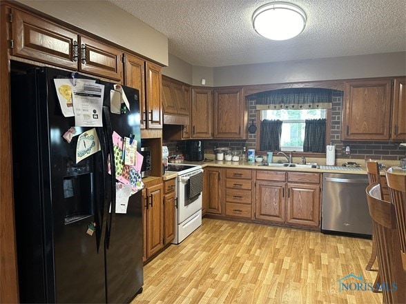 kitchen with electric range, dishwasher, tasteful backsplash, black fridge, and light wood-type flooring