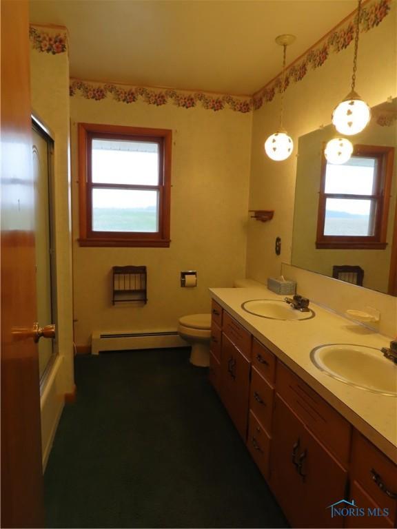 full bathroom featuring vanity, plenty of natural light, a baseboard heating unit, and enclosed tub / shower combo