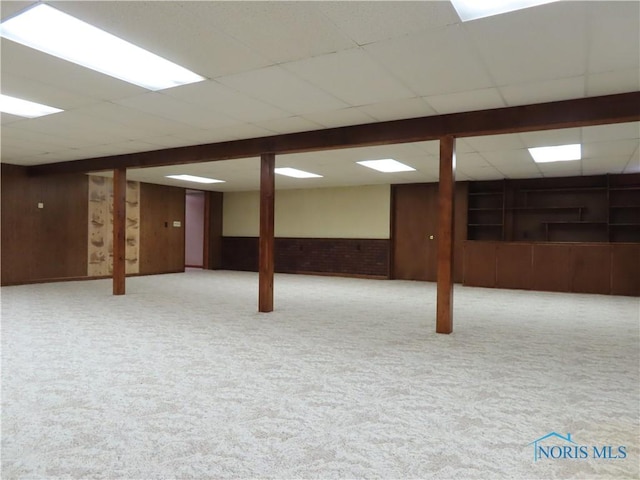 basement with light carpet, a drop ceiling, and wooden walls