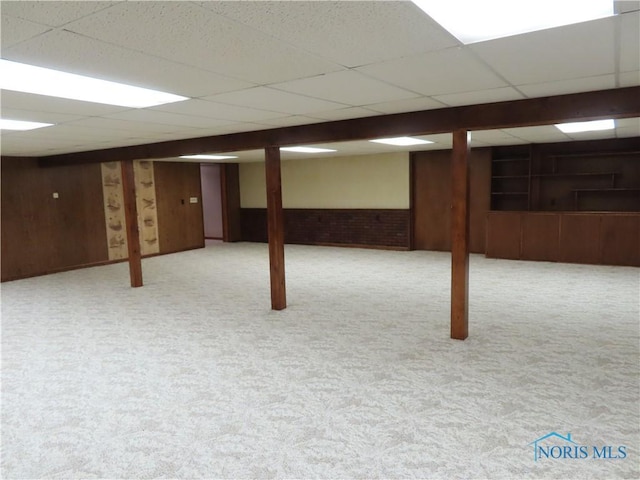 basement featuring a paneled ceiling, light carpet, and wooden walls