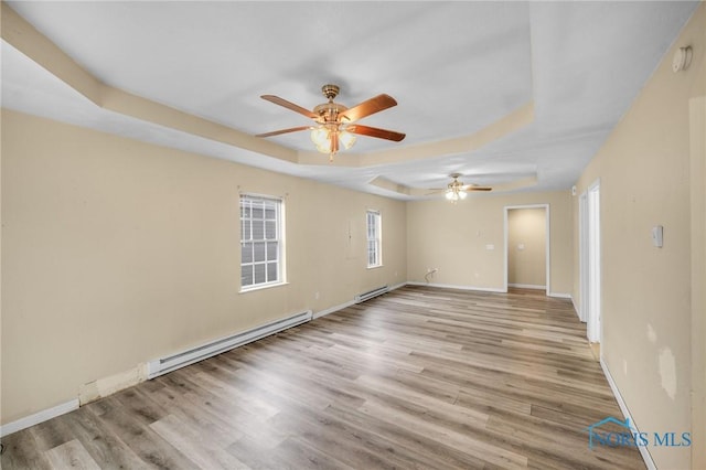 empty room with a raised ceiling, light wood-type flooring, and a baseboard radiator