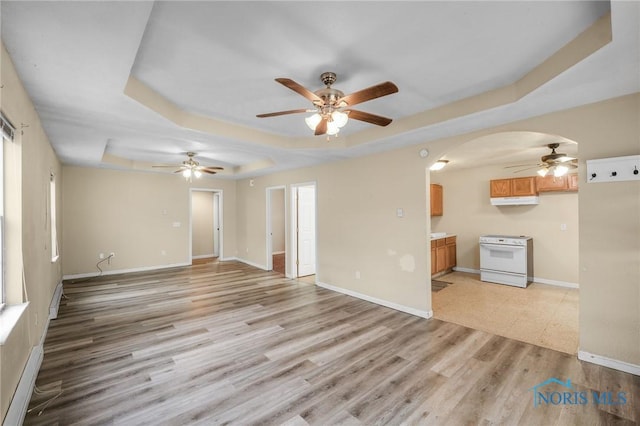 unfurnished living room featuring a tray ceiling, ceiling fan, and light hardwood / wood-style flooring