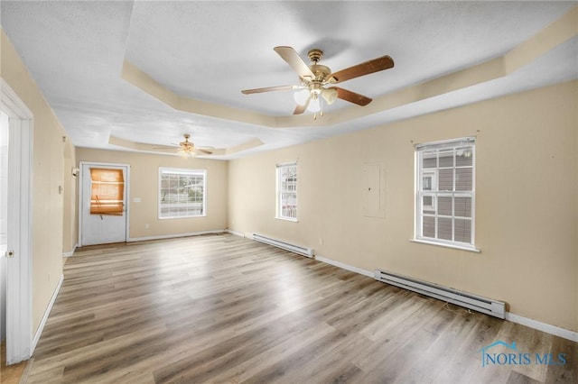 spare room featuring a raised ceiling, light hardwood / wood-style flooring, and a baseboard heating unit