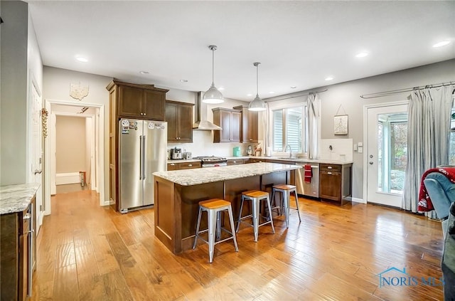 kitchen featuring light stone countertops, appliances with stainless steel finishes, light hardwood / wood-style flooring, a kitchen island, and a breakfast bar area