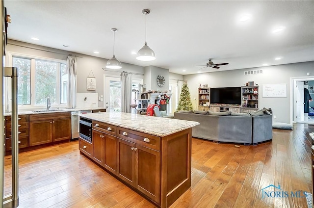 kitchen featuring light stone countertops, light wood-type flooring, ceiling fan, pendant lighting, and a kitchen island