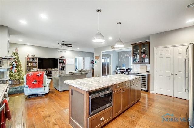 kitchen featuring light wood-type flooring, stainless steel microwave, ceiling fan, a kitchen island, and hanging light fixtures