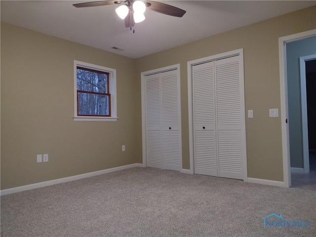 unfurnished bedroom featuring multiple closets, ceiling fan, and light carpet