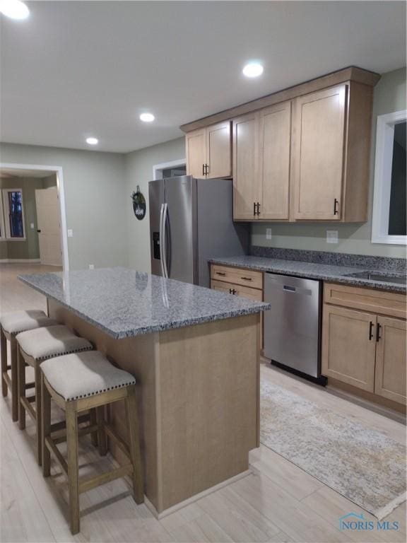 kitchen featuring a kitchen bar, stainless steel appliances, light brown cabinetry, and light hardwood / wood-style flooring