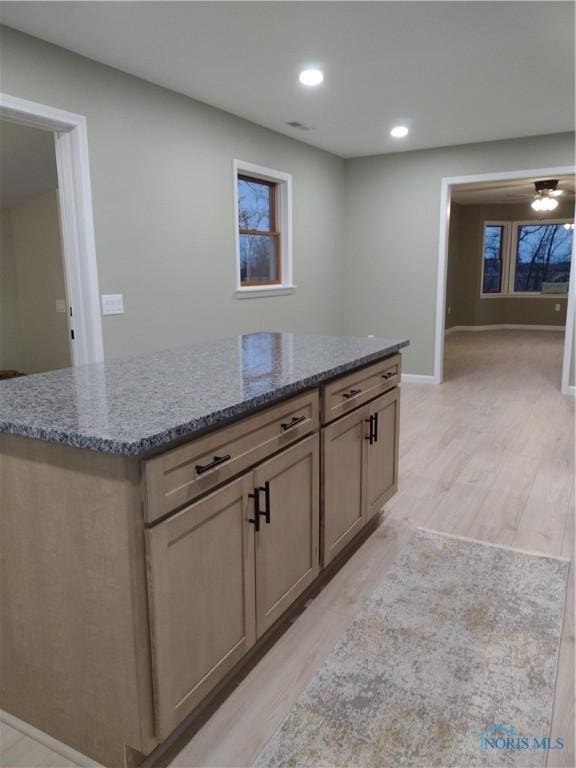 kitchen with a center island, light hardwood / wood-style flooring, ceiling fan, and light stone counters