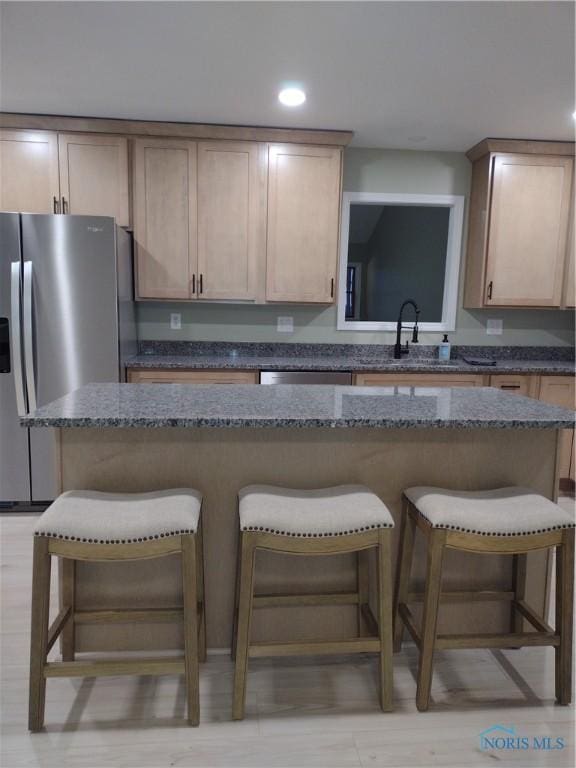 kitchen featuring sink, a breakfast bar area, light brown cabinetry, and dark stone counters